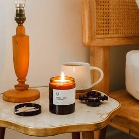 Handmade Candle Co. Amber & Musk Soy Wax Candle sat on bedside table next to a mug