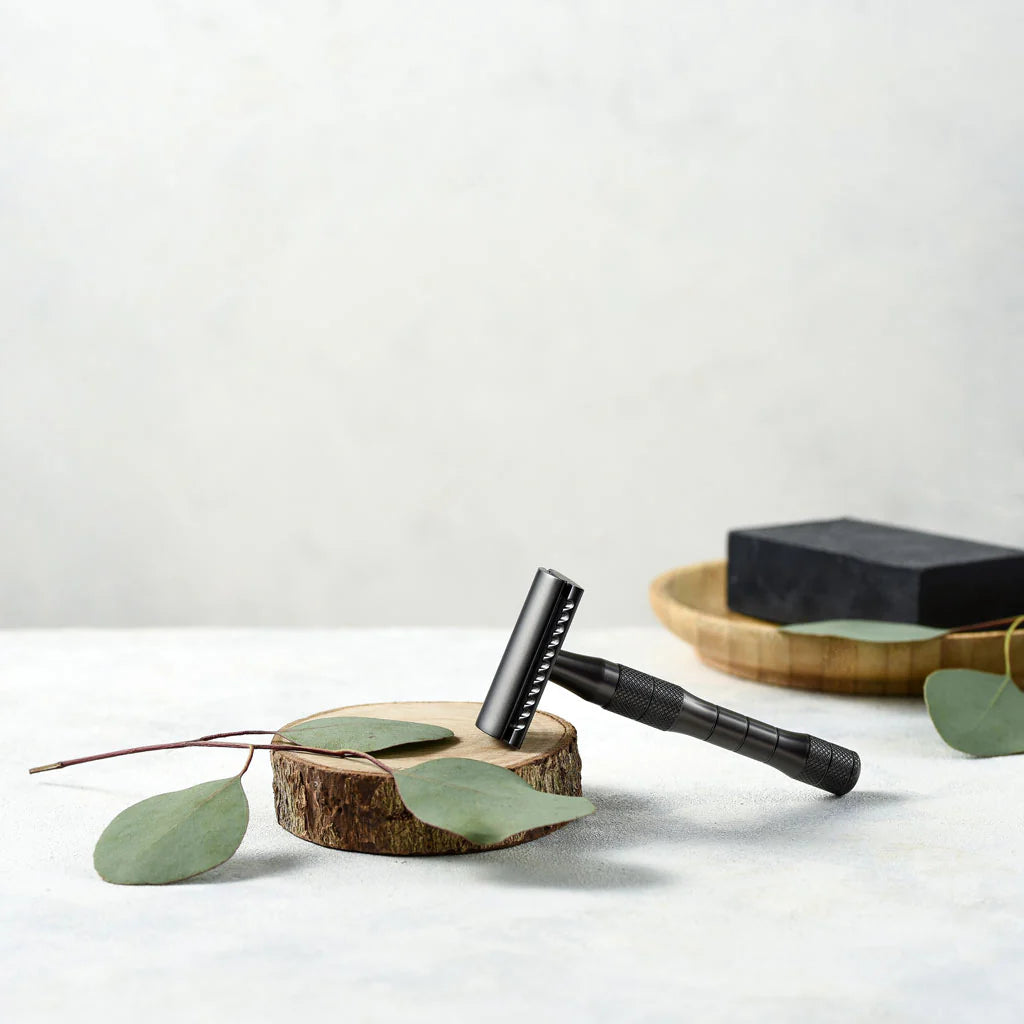 Metallic black reusable safety razor with ergonomic handle on table next to shving soap
