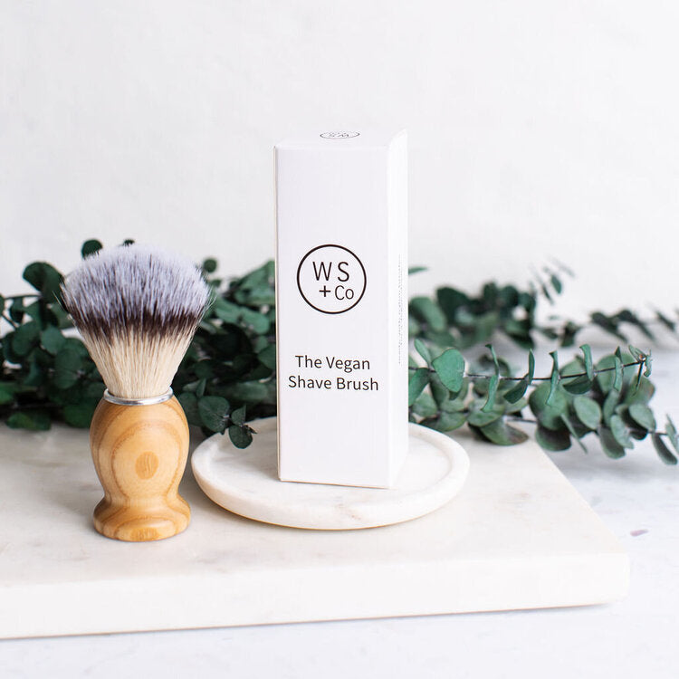 Wild Sage + Co. Wooden Shave Brush next to box stood on marble coaster and near eucalyptus