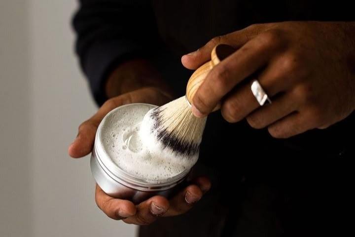 Wild Sage + Co. shaving soap in travel tin being used with the vegan wooden shave brush